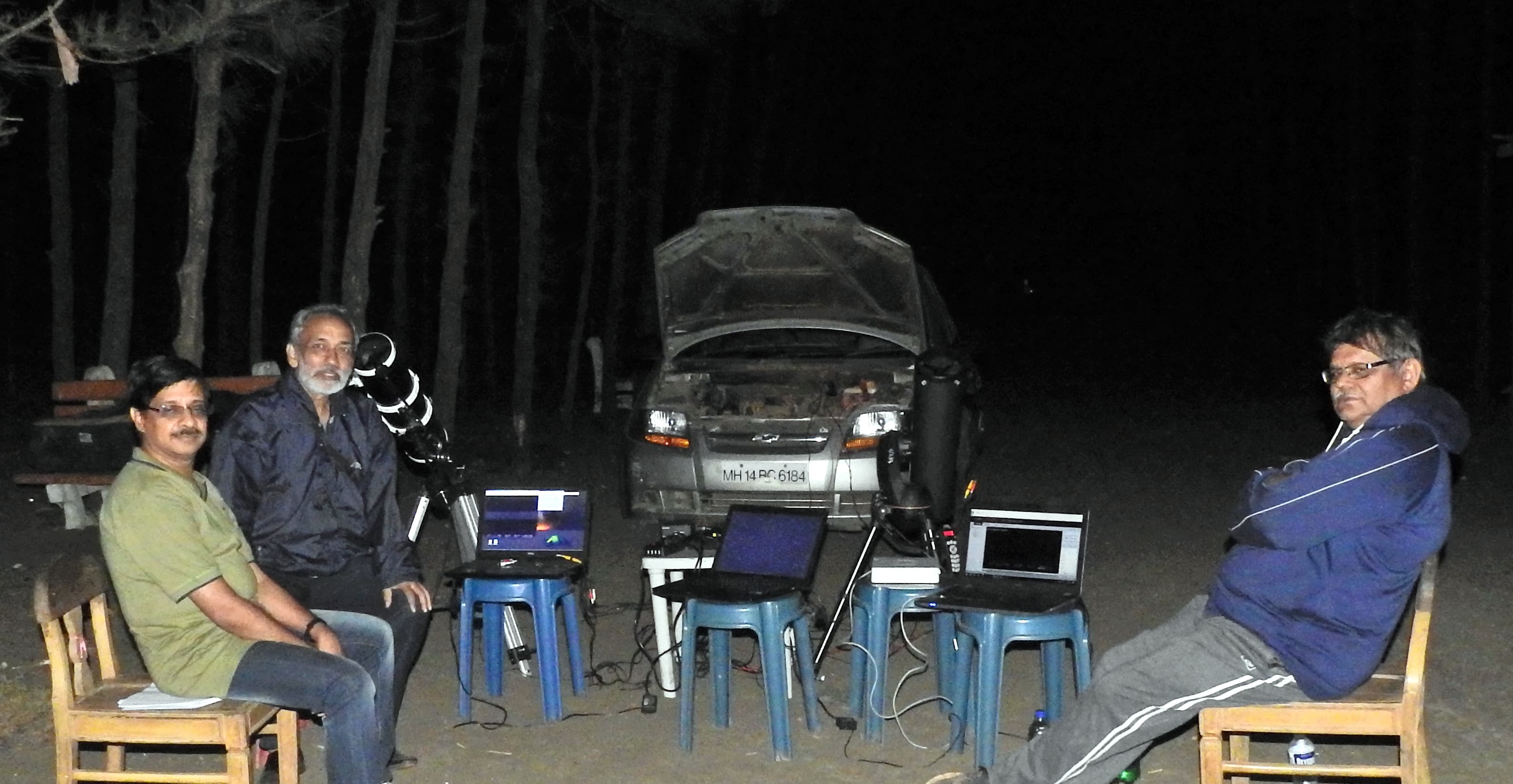 Three observers seated beside telescopes and laptops at night